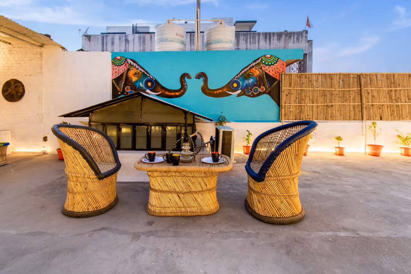 Terrace dining set with cane chairs beneath a folk-art mural at Polaris Art Terrace, Jaipur