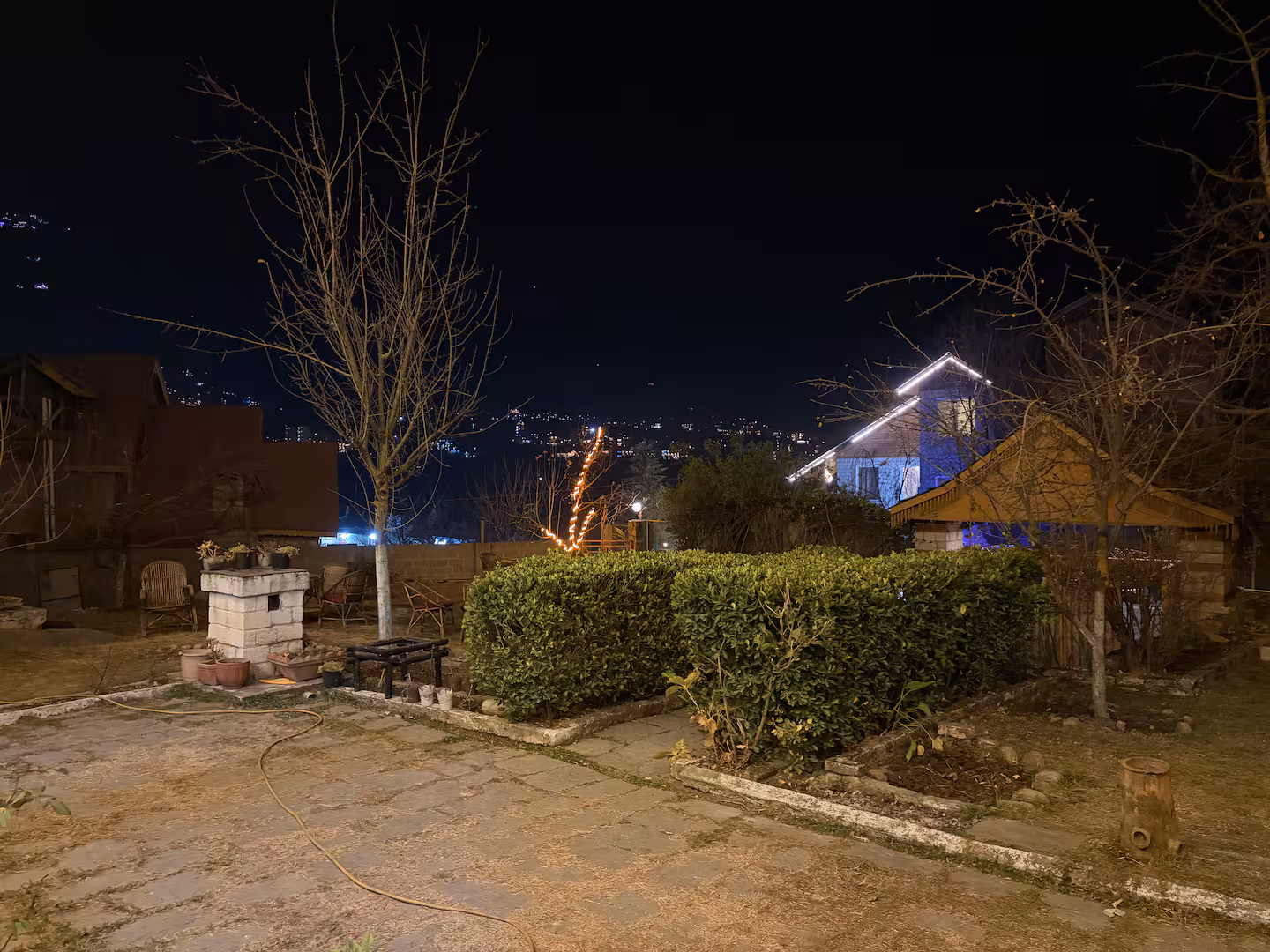 Courtyard and lawn at night with hillside lights beyond at Polaris Himalayan Chalet, Manali