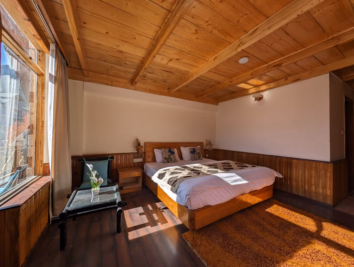 Sunlit bedroom with timber ceiling and wide windows at Polaris Himalayan Chalet, Manali