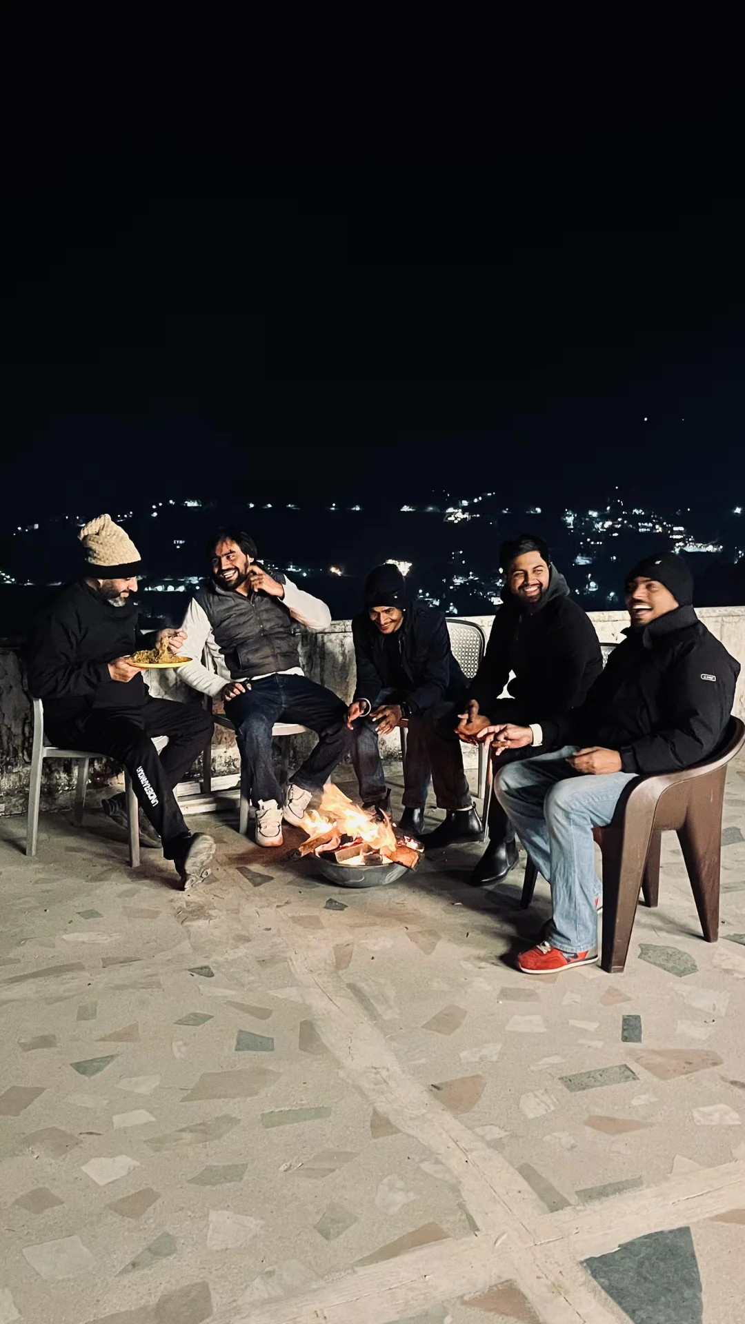 Guests gathered around a bonfire on the terrace with city lights below at Polaris Alpine, Mussoorie