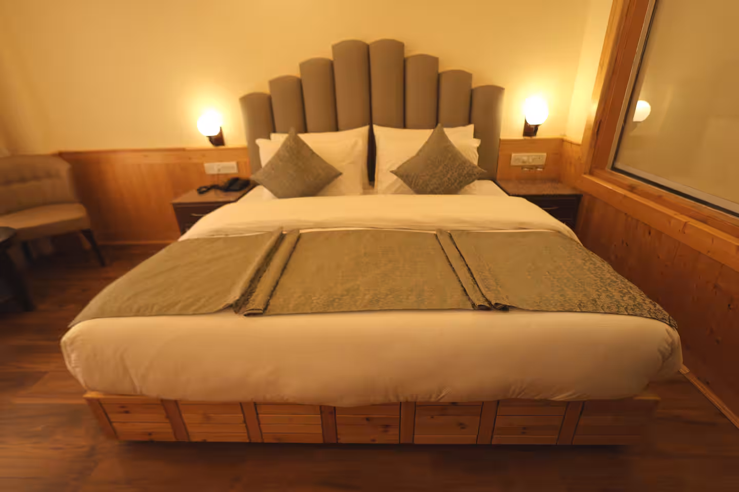 King bed with bedside lamps and pine panelling in a guest room at Polaris Golden Wood, Manali