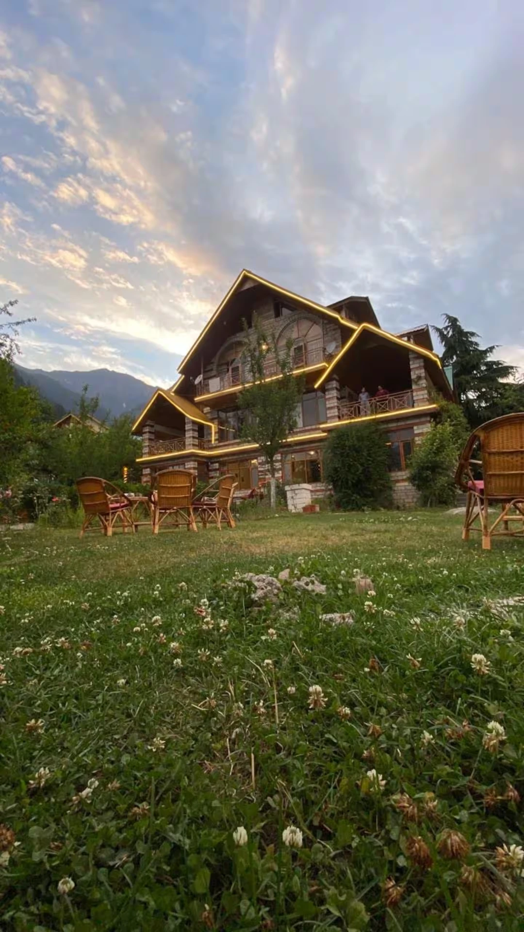 Stone and timber facade of Polaris Himalayan Chalet at sunset with lawn seating, Simsa, Manali