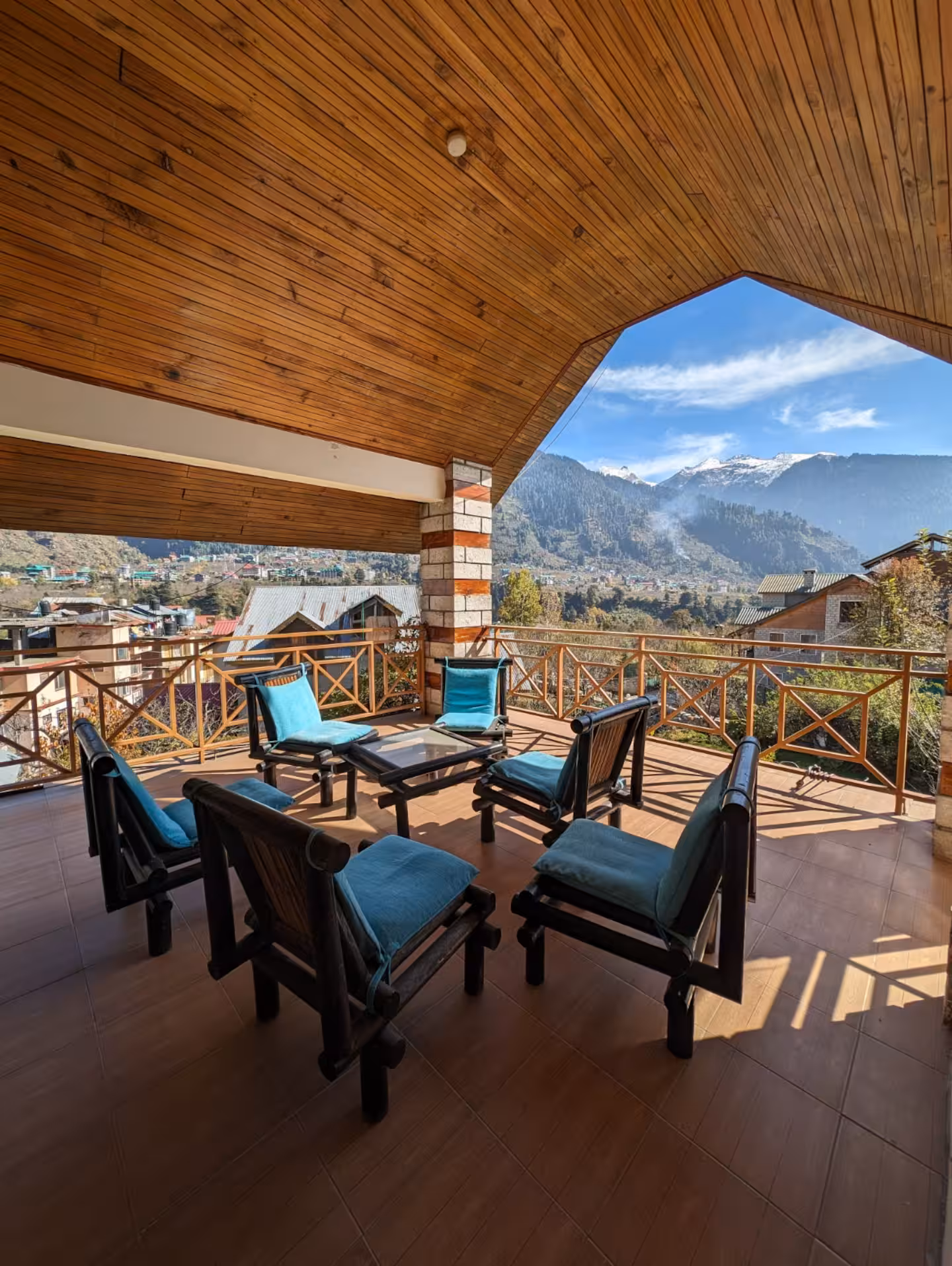 Covered balcony lounge with wooden ceiling and snow-capped mountain views at Polaris Himalayan Chalet, Manali
